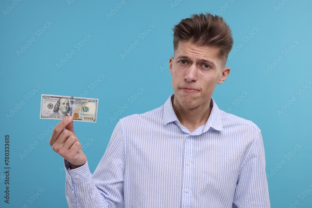 Upset man with dollar banknote on light blue background Upset man with dollar banknote on light blue background