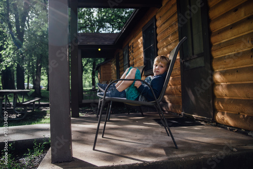 Young boy sitting on chair on porch of cabin in summer photo