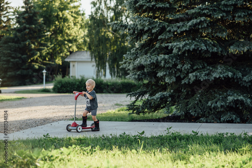 Wide view of boy riding scooter outside in driveway in summer photo