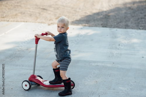 Small toddler riding scooter outside in driveway in summer photo