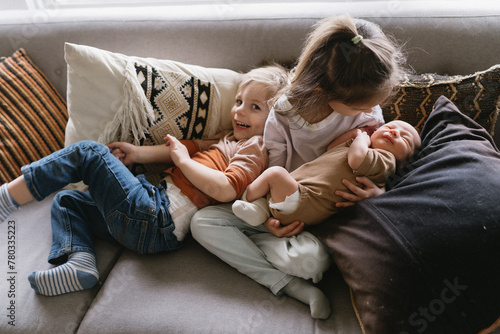 a growing family of siblings snuggling on the couch with newborn photo