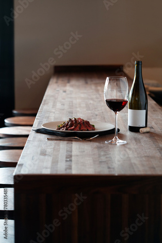 A plated meat entree served with a glass of red wine on a bar table