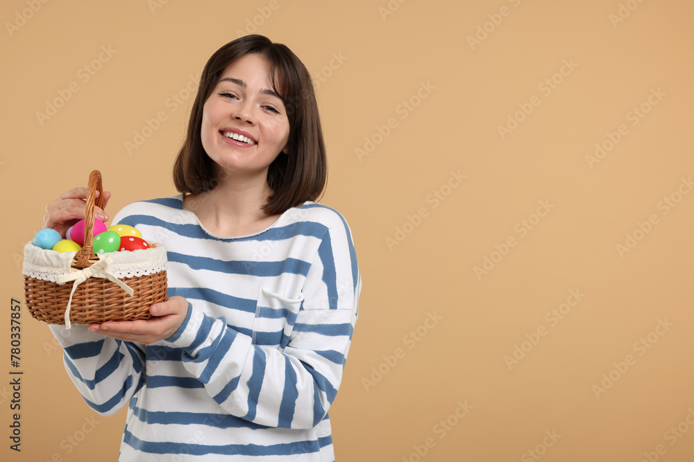 Easter celebration. Happy woman with wicker basket full of painted eggs on beige background, space for text Easter celebration. Happy woman with wicker basket full of painted eggs on beige background, space for text
