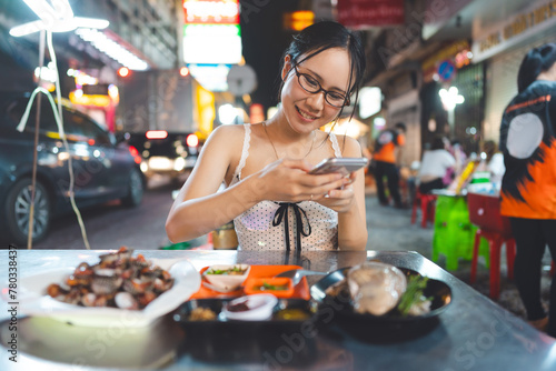 Asian foodie tourist woman eating raw oyster seafood at China town asia street food night market photo