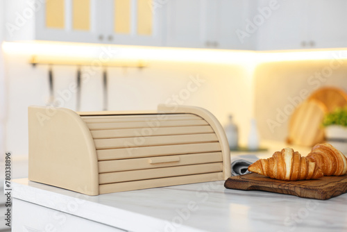Wooden bread box and board with croissants on white marble table in kitchen photo