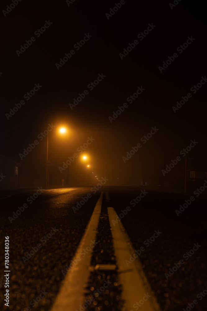 Misty, foggy night time road with the soft glow of yellow street lights leading you off into the distance. Misty, foggy night time road with the soft glow of yellow street lights leading you off into the distance.