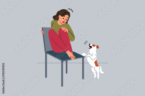 Teenage girl is afraid of dog and climbs onto chair to hide from puppy and needs treatment for cynophobia. Kid feels panic attack at sight of pets due to cynophobia or possibility of allergic reaction