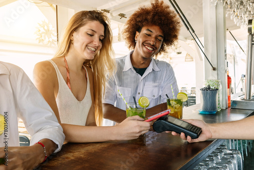 Young couple using contactless credit or debit card for payment at beach bar