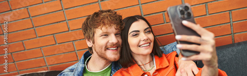 Man and woman smiling, posing, and using a cell phone to take a selfie together in a joyful moment of connection and companionship
