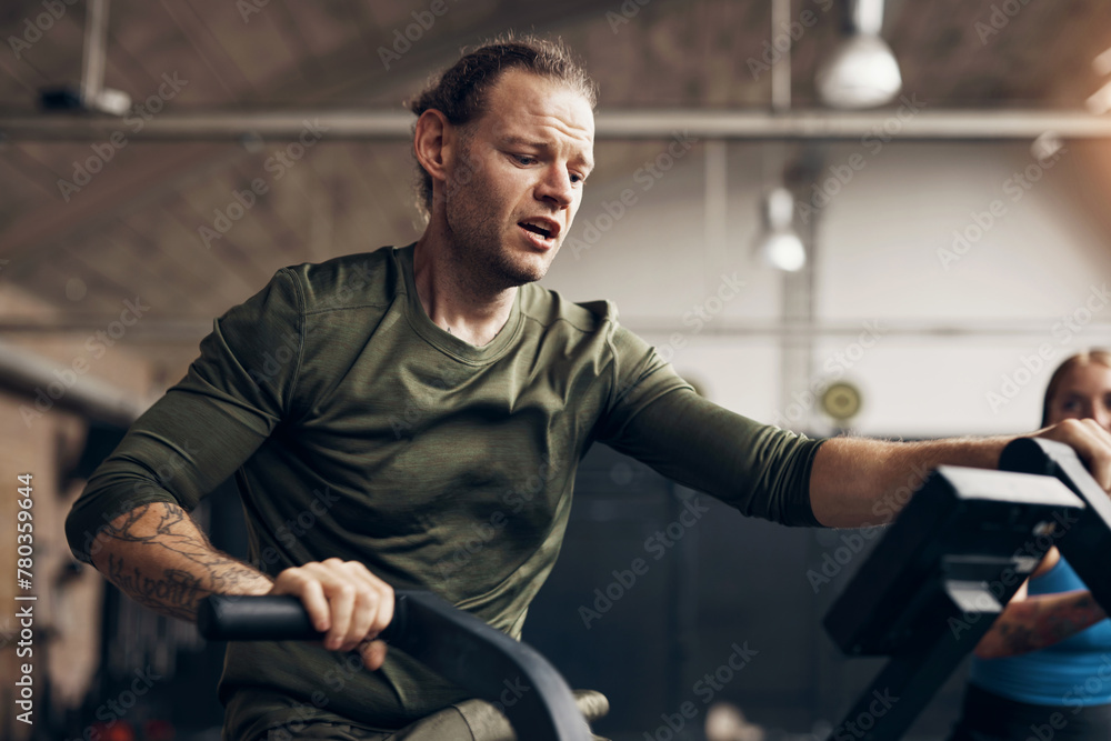 Fit man exercising on a stationary bike at the gym. He has sweat on his forehead and is focused on his workout. Fit man exercising on a stationary bike at the gym. He has sweat on his forehead and is focused on his workout.