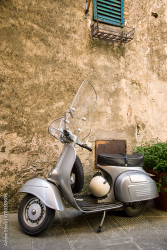 A vintage scooter stands parked by a weathered wall, its classic design and accompanying helmet painting a picture of timeless adventure in a serene alleyway photo