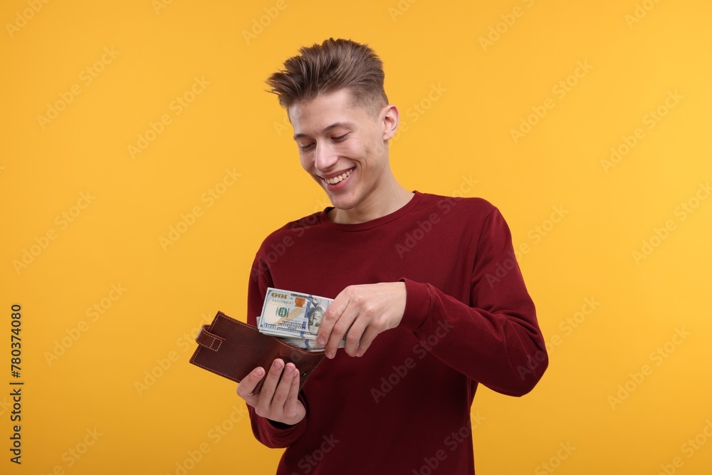 Happy man putting money into wallet on yellow background Happy man putting money into wallet on yellow background