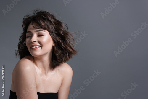 Portrait of beautiful young woman with wavy hairstyle on grey background. Space for text