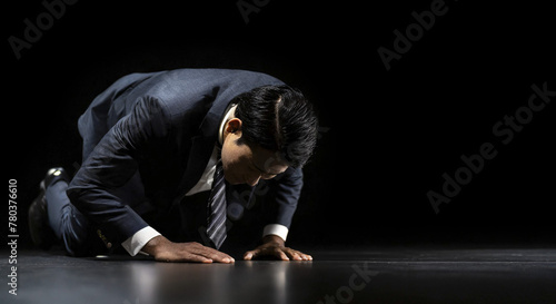 失敗し暗い部屋で跪き項垂れ絶望するスーツを着た仕事中のビジネスマンの日本人男性　後悔・謝罪・増税・落ち込む・鬱・破産のイメージ photo
