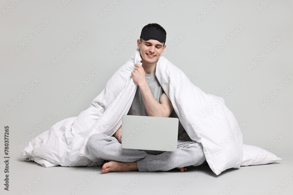 Happy man in pyjama wrapped in blanket using laptop on grey background Happy man in pyjama wrapped in blanket using laptop on grey background