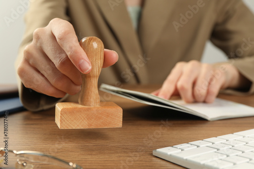 Woman with stamp and passport at wooden table, closeup