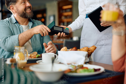 Close up of man paying contactless with mobile phone while having breakfast in  hotel.