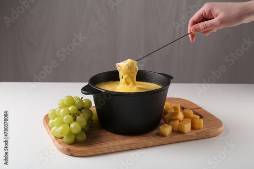 Woman dipping piece of bread into fondue pot with tasty melted cheese at white table, closeup