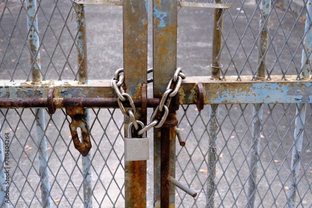 Rusty iron door with mesh fences locked with a new metal chain and a padlock Rusty iron door with mesh fences locked with a new metal chain and a padlock