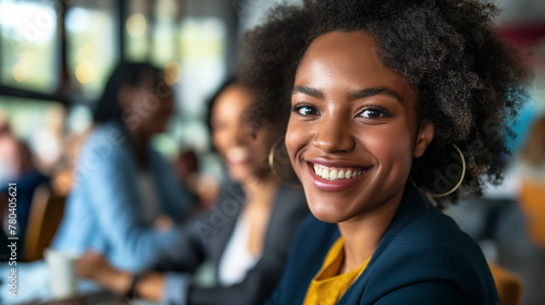 Cheerful young woman with curly hair smiles brightly at a cafe, with people in the background.