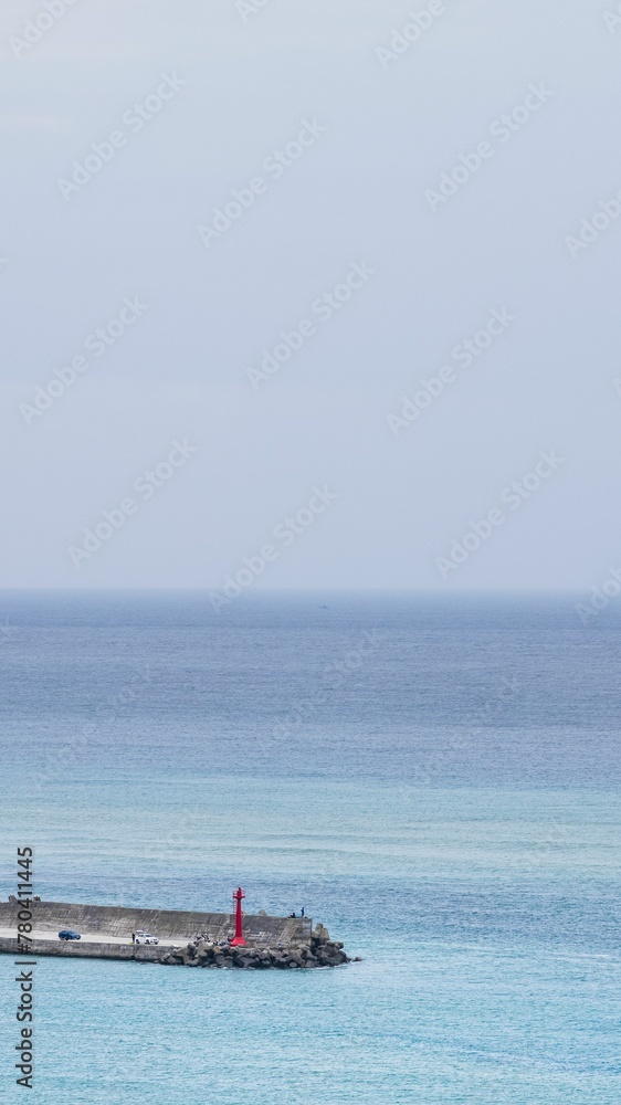 Vertical aerial shot of pier with red lighthouse surrounded by sea water under blue sky