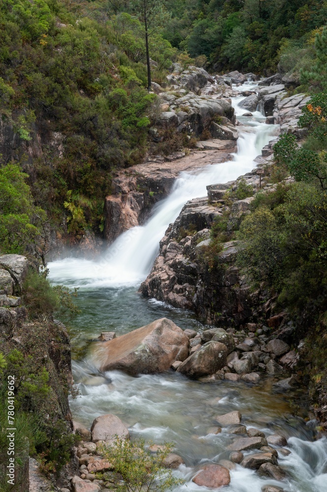 Fototapeta premium Vertical shot of the flowing rocky waterfall in Peneda-Geres National Park in Portugal