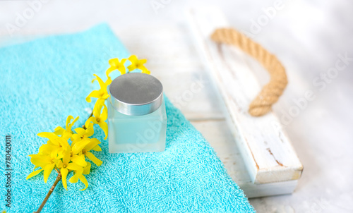 a jar of cream and a blooming branch with yellow flowers on an emerald towel. spa and freshness atmosphere