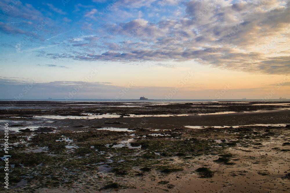 Landscape view of a sunrise over the beach at low tide against a clouded sky