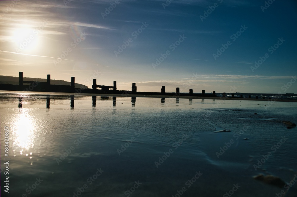 Beautiful view of the breakwater with reflection in the sea in Sandow bay, Isle of Wight at sunset - obrazy, fototapety, plakaty 