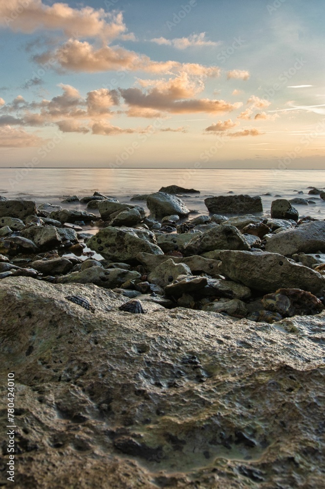Vertical shot of a beach full of rocks with a calm sea in the background in the evening