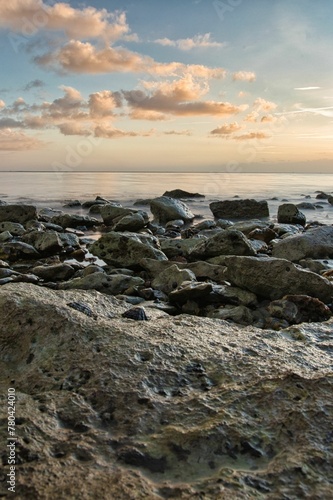 Vertical shot of a beach full of rocks with a calm sea in the background in the evening