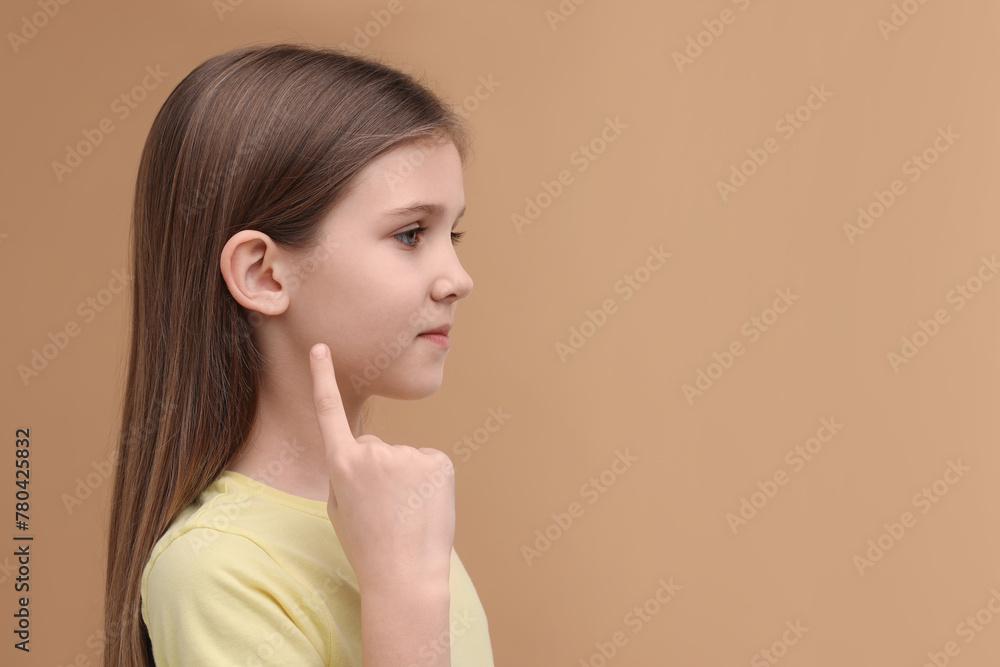 Hearing problem. Little girl pointing at ear on pale brown background, space for text Hearing problem. Little girl pointing at ear on pale brown background, space for text