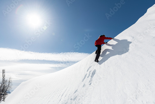 Low angle view of woman climbing up on powdered snow hill against blue sky during sunny day photo