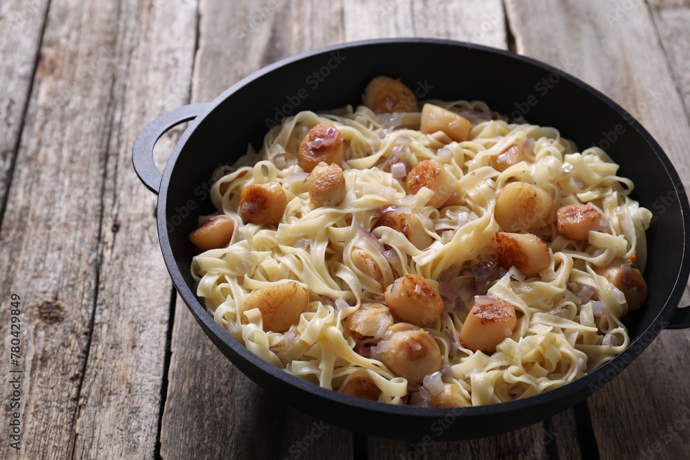 Delicious scallop pasta with onion in pan on wooden table, closeup Delicious scallop pasta with onion in pan on wooden table, closeup