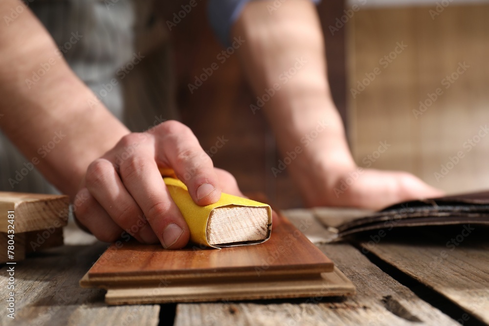 Man polishing wooden plank with sandpaper at table indoors, closeup - obrazy, fototapety, plakaty 