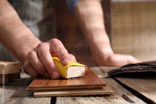 Man polishing wooden plank with sandpaper at table indoors, closeup photo