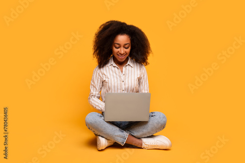 Woman sitting with laptop on floor on yellow background photo