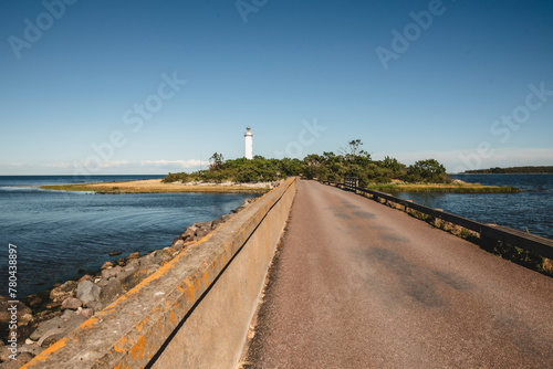 Empty road leading to lighthouse by sea against blue sky photo