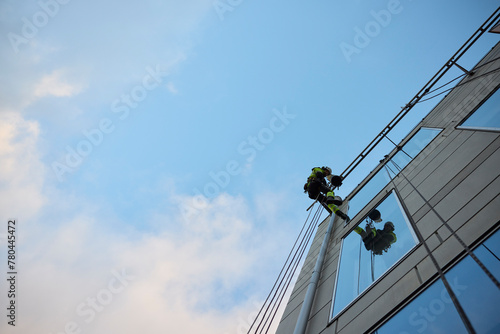 Low angle view of male rope access worker hanging on glass building under blue sky