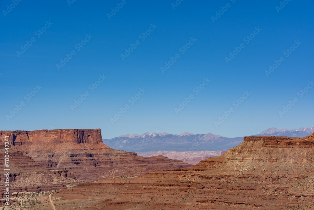 Peaceful desert landscape in a canyon with dry brown fields and rocky cliffs under a clear blue sky