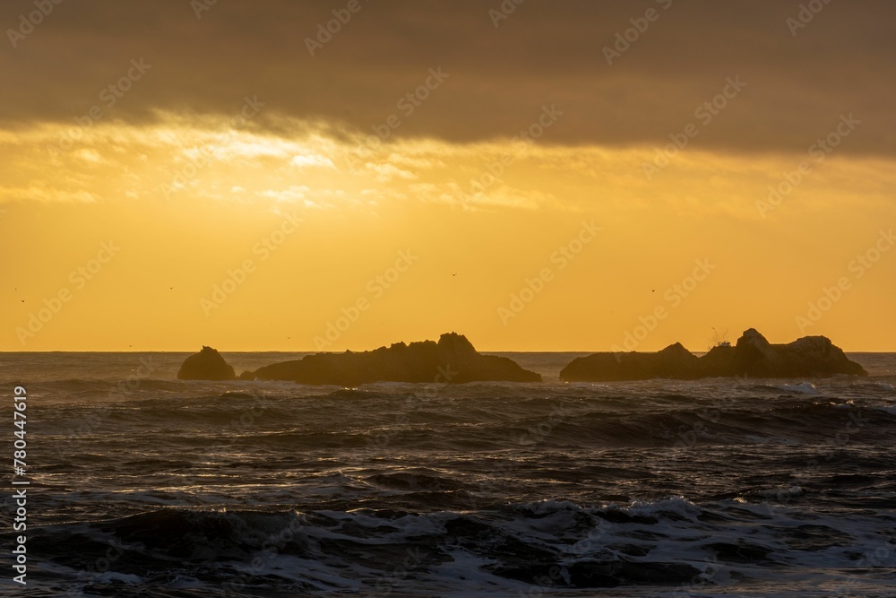 Lovely seascape during a golden sunset with low stormy waves washing over jagged rocks in the water