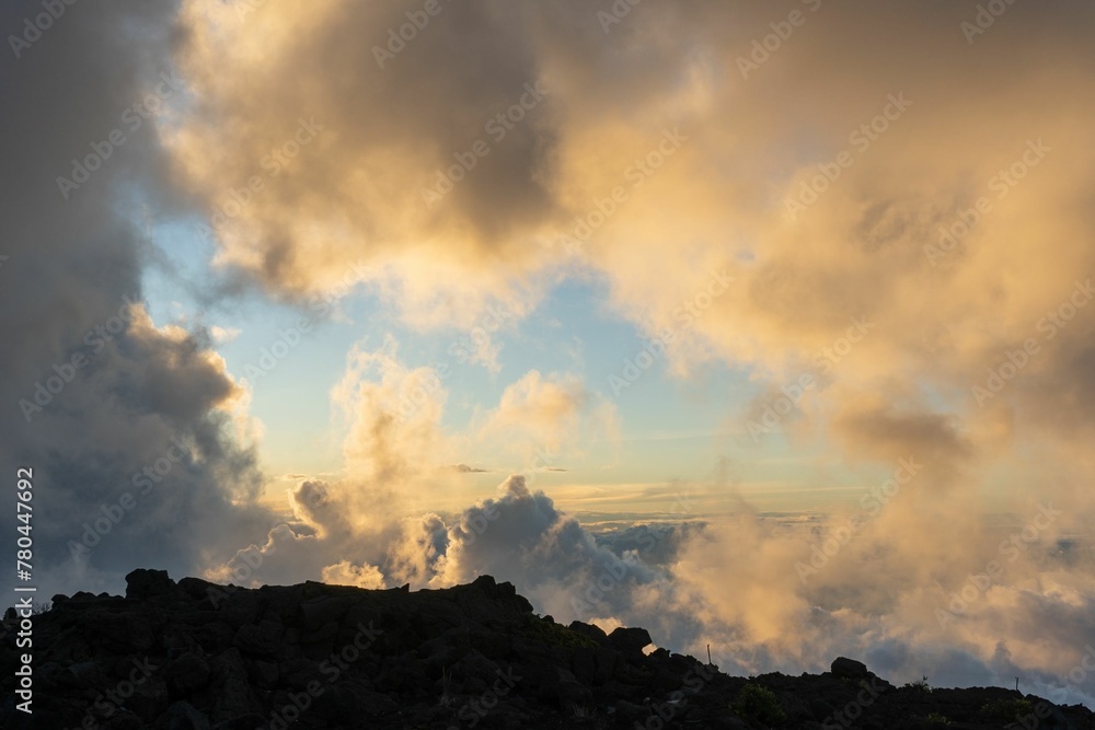 Swarm of soft cotton-like clouds circling around a mountain peak under gentle pink-gold sunlight