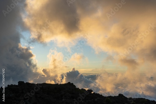 Swarm of soft cotton-like clouds circling around a mountain peak under gentle pink-gold sunlight