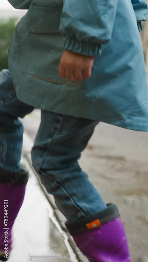 Child in rubber boots jumps on sidewalk. Kid playful spirit undampened by wet conditions near building. Simple pleasures of outdoor play after rain Child in rubber boots jumps on sidewalk. Kid playful spirit undampened by wet conditions near building. Simple pleasures of outdoor play after rain