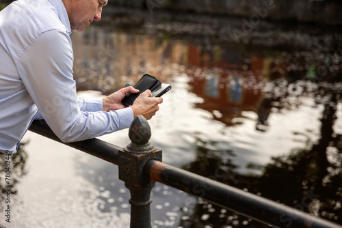 Man leaning on railing and using smart phone against river photo