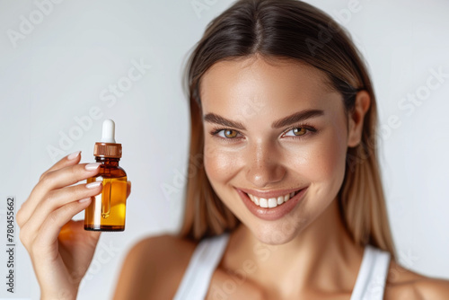 Radiant young woman with a gleaming smile presenting a skincare oil dropper bottle photo
