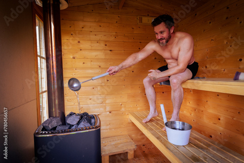 Smiling mature man pouring water on stones in sauna photo