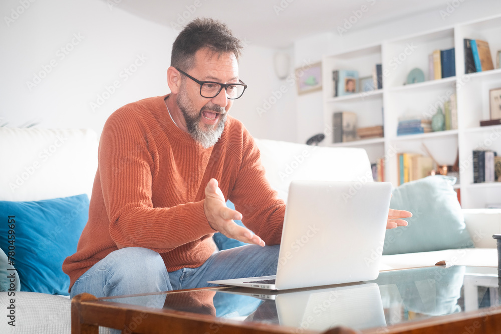 Smiling senior man wear glasses gesturing to camera having video call on laptop, happy adult male enjoy computer connection sit on couch at home talk using modern technologies and wireless connection Smiling senior man wear glasses gesturing to camera having video call on laptop, happy adult male enjoy computer connection sit on couch at home talk using modern technologies and wireless connection