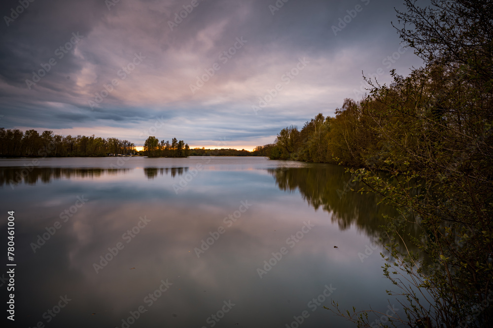 Beautiful sunset over the lake surrounded by trees which reflect in the water in Bavaria, Germany