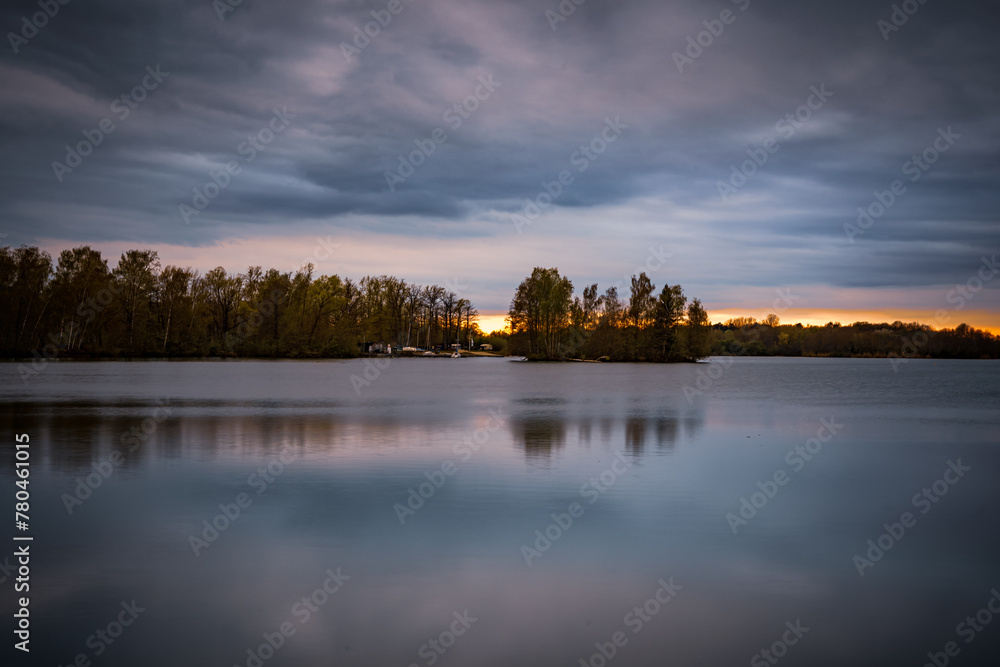 Beautiful sunset over the lake surrounded by trees which reflect in the water in Bavaria, Germany Beautiful sunset over the lake surrounded by trees which reflect in the water in Bavaria, Germany